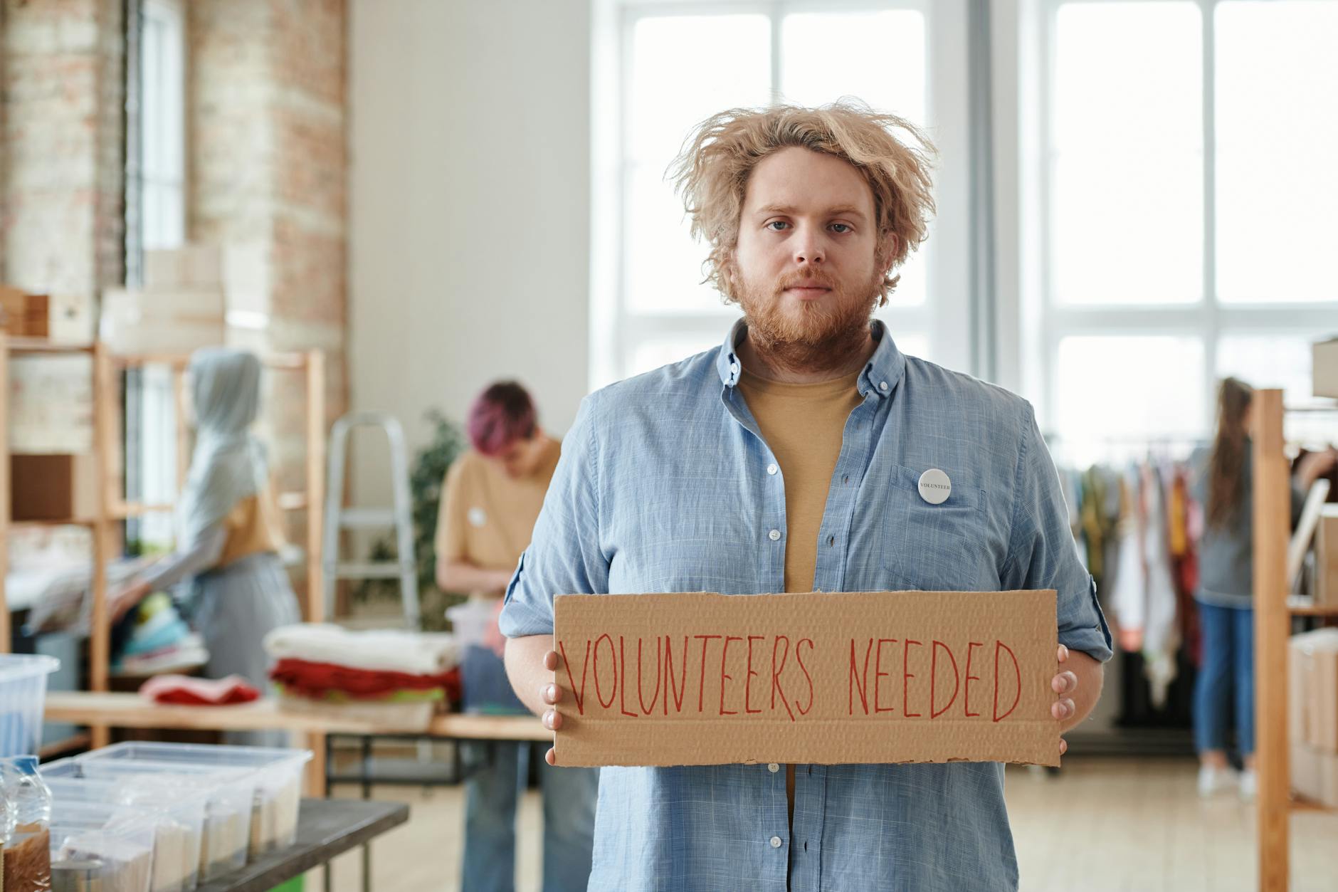 Man holding a sign for volunteer recruitment at a community center.