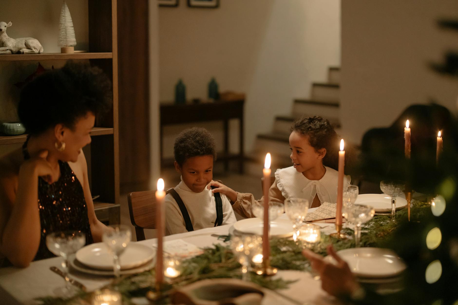 Family gathering around a decorated dining table with lighted candles for a Christmas celebration.